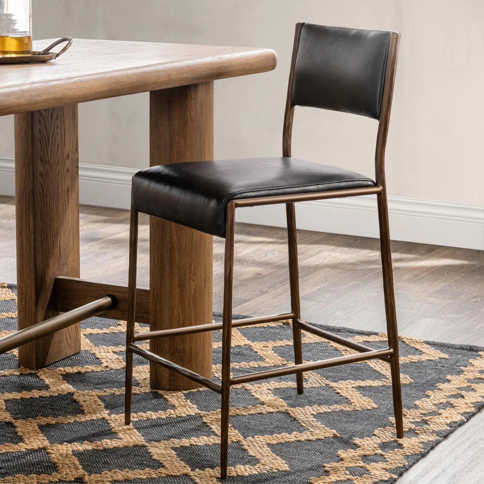 Kayne leather counter stool beside a warm wood counter-height table on a patterned woven rug