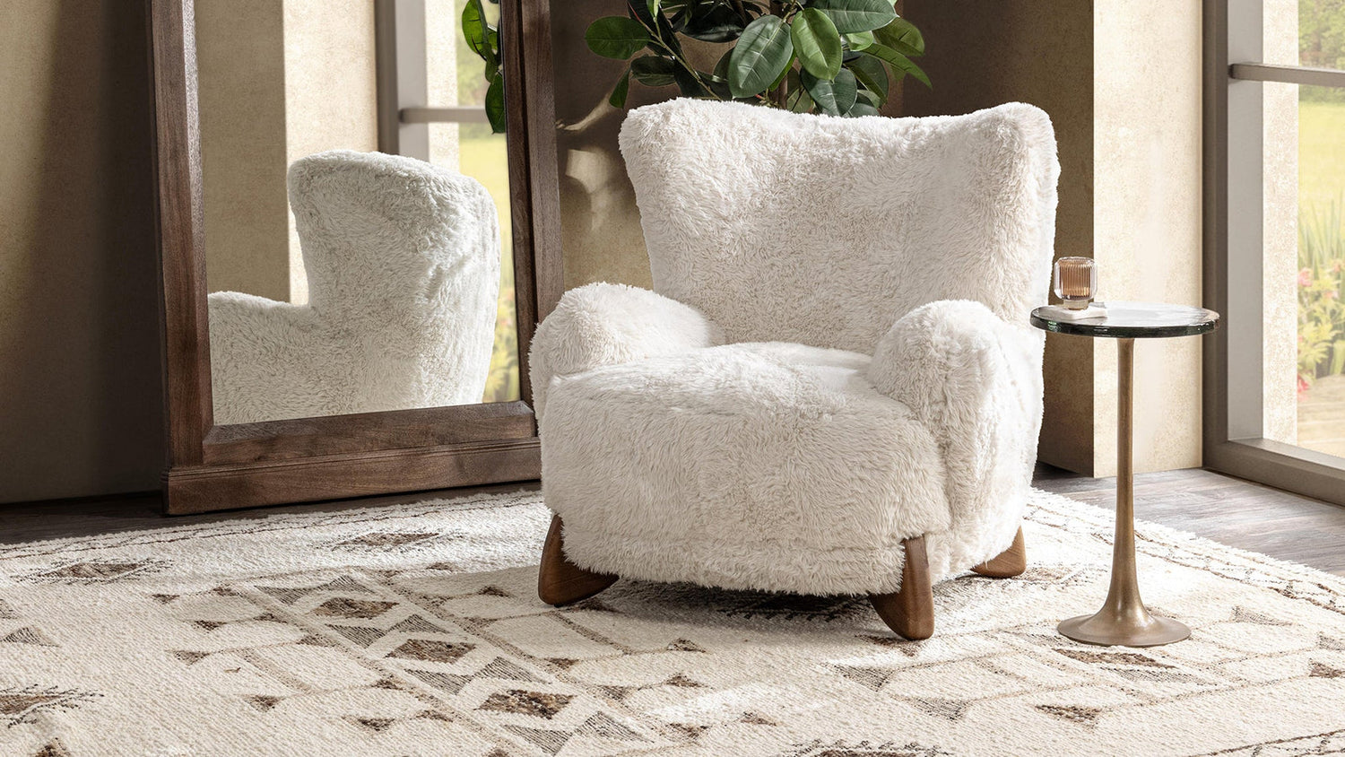 Riya accent chair in a warm neutral living room with a wood mirror, side table, greenery, and layered rug