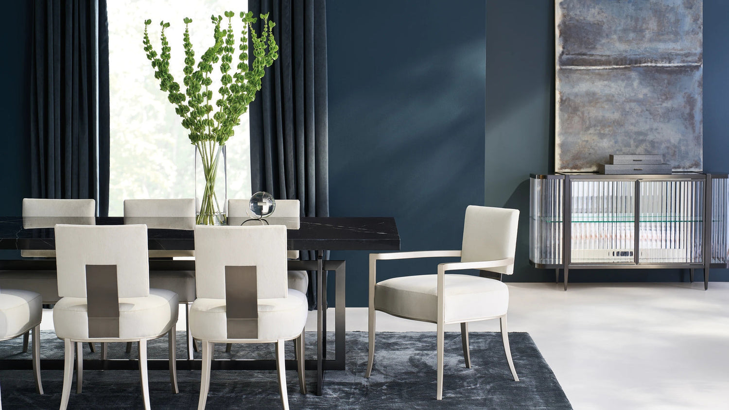 Caracole dining room with a dark dining table, white upholstered chairs and a mirrored sideboard