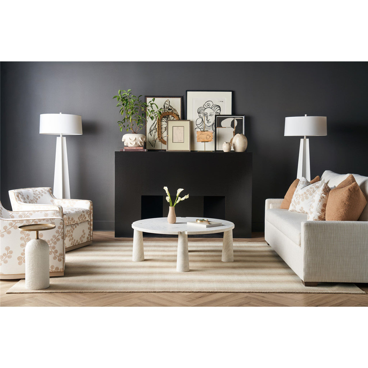 Styled living room with a round coffee table, sofa, lounge chair, lamps, artwork, and neutral rug