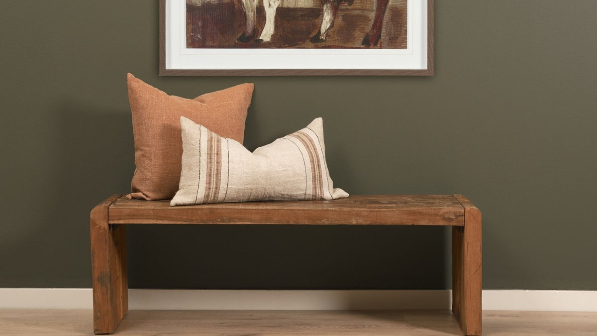 Reclaimed wood bench styled with pillows beneath framed art in a warm entryway