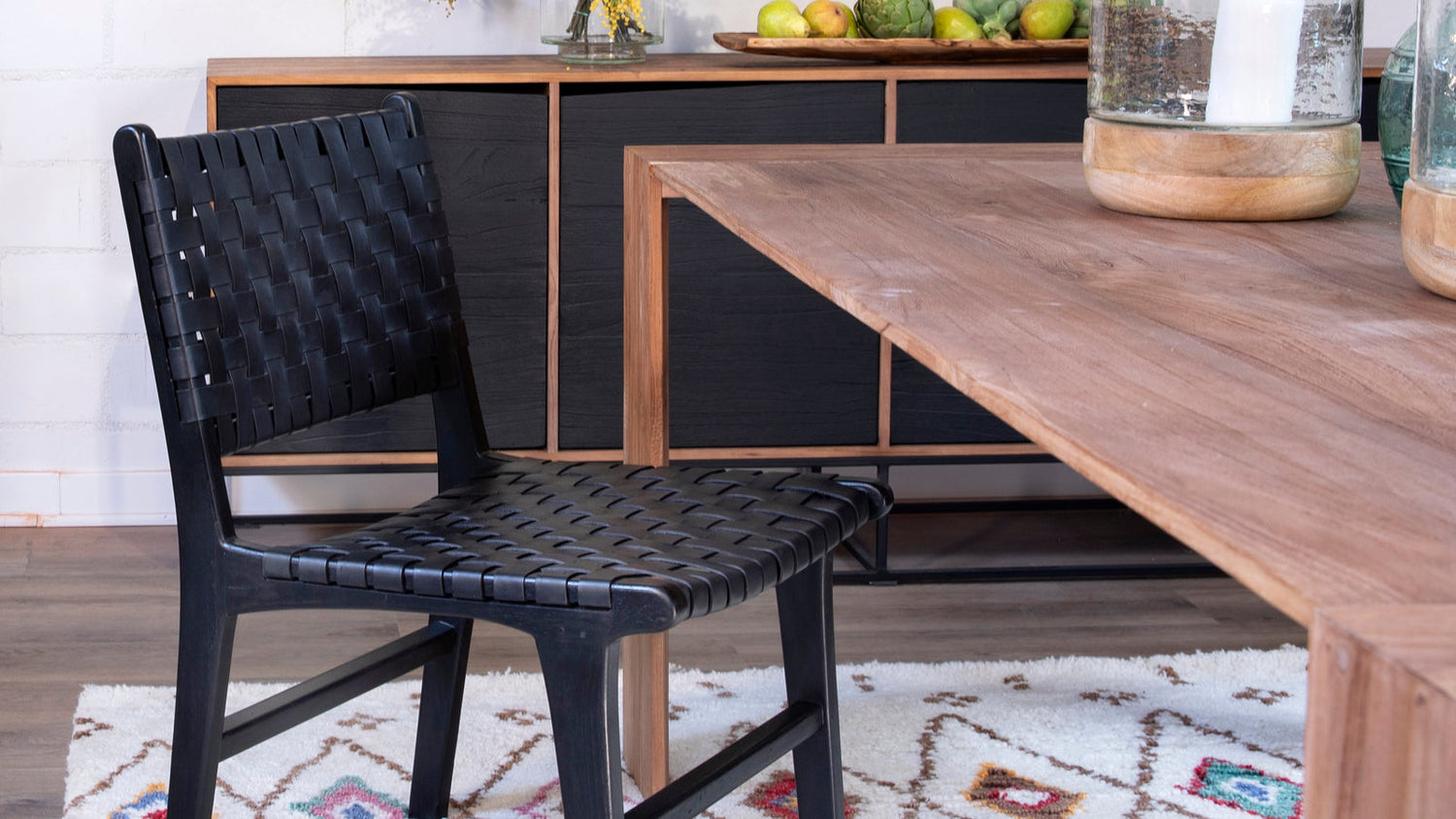 Black woven leather dining chair beside a wood table on a patterned area rug