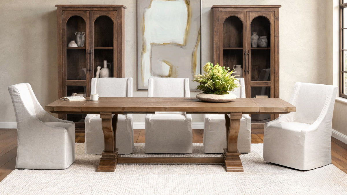 Reclaimed wood dining table with white slipcovered chairs and tall wood cabinets