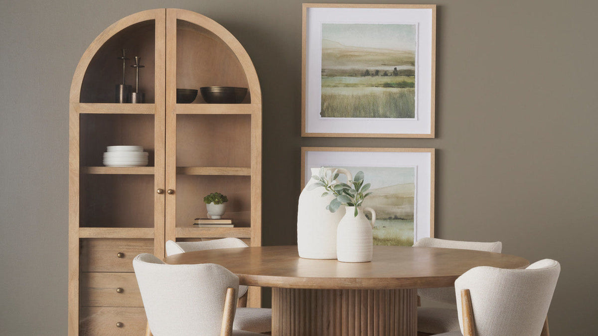 Light brown arched glass-door curio cabinet styled with tableware beside a round dining table