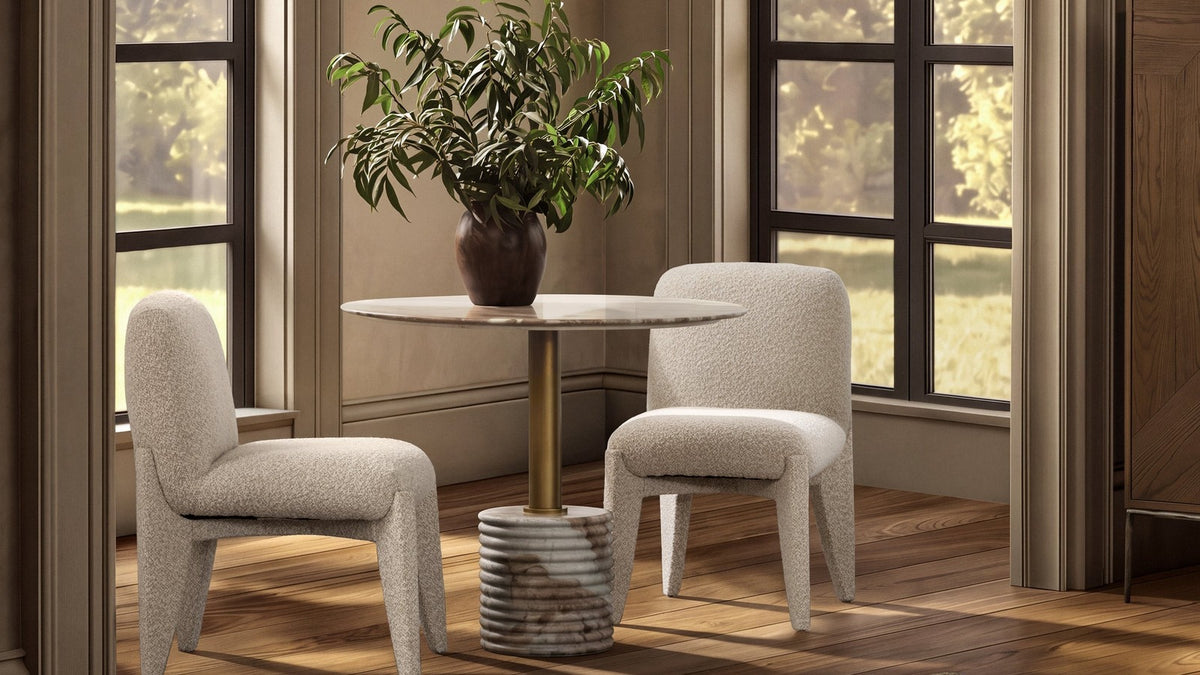 Small round marble dining table with two upholstered chairs in a sunlit room