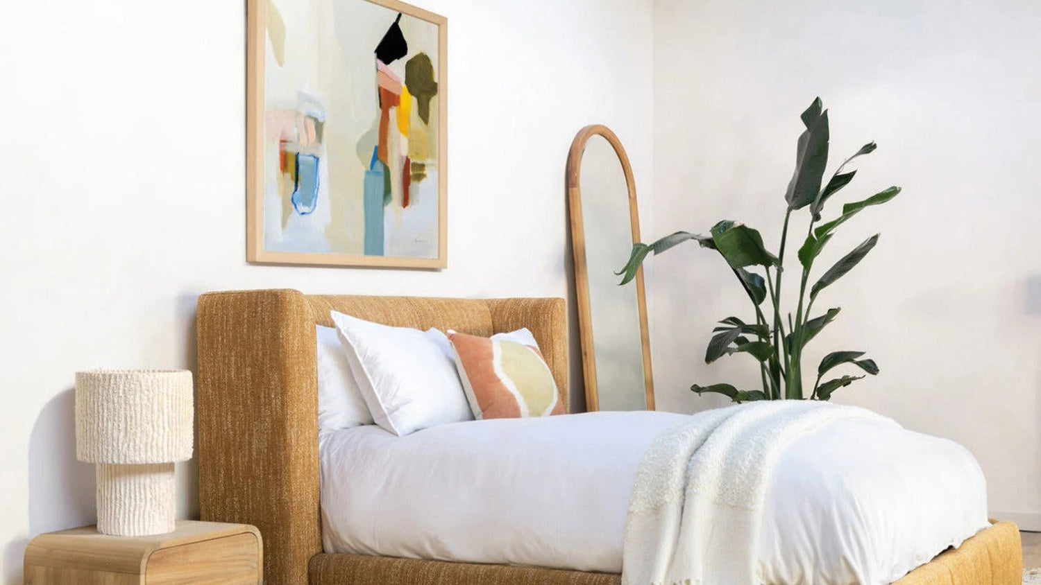 Mustard boucle upholstered platform bed styled with white bedding in a modern bedroom