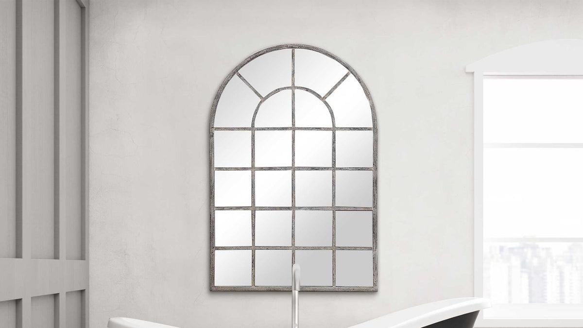 Arched windowpane mirror styled above a freestanding tub in a bright bathroom
